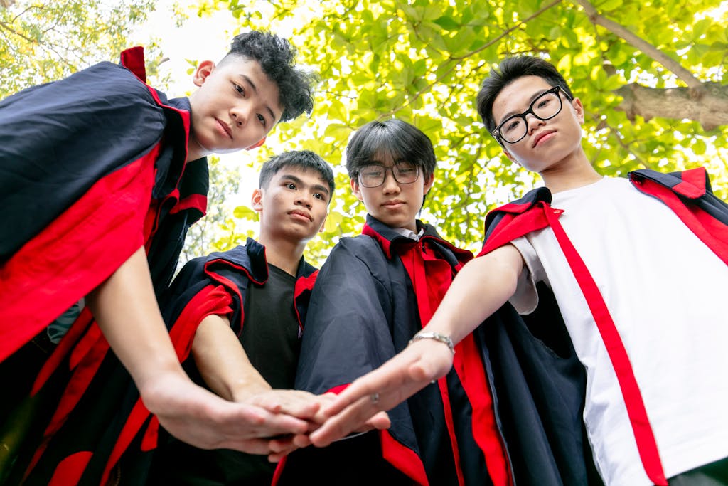 A group of college graduates celebrating teamwork and unity outdoors under a bright sky.