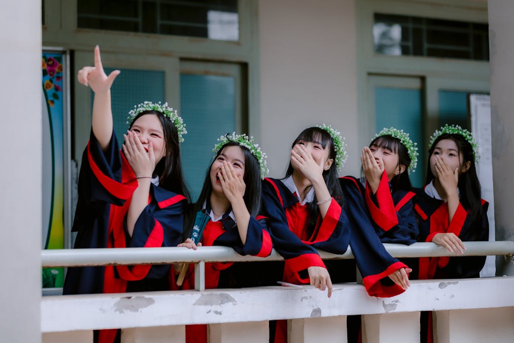 Group of five female graduates in gowns laughing and celebrating with joy.