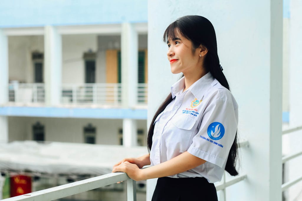 Smiling Asian woman in a school uniform standing outdoors on a balcony.