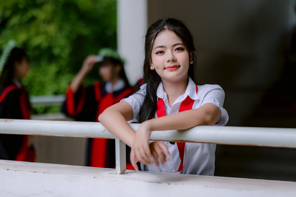 Smiling young woman in school uniform poses during an outdoor graduation ceremony.
