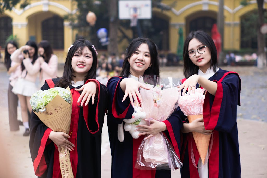 Three young women celebrate graduation outdoors with bouquets and joyful smiles.